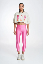 Woman wearing a white cropped top with colorful letters and pink leggings on a white background