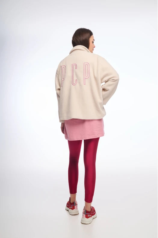 Person wearing a cream jacket with 'DCP' branding, pink skirt, and red leggings on a white background