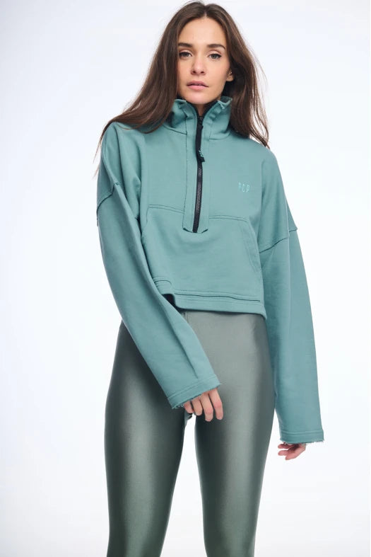 Woman wearing a teal pullover with a black zipper on a white background