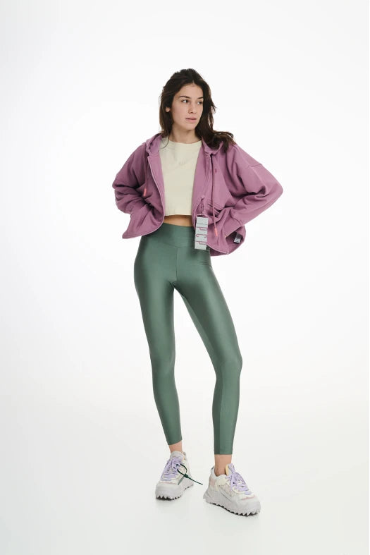 Person wearing a pink jacket, white shirt, green leggings, and white sneakers on a white background