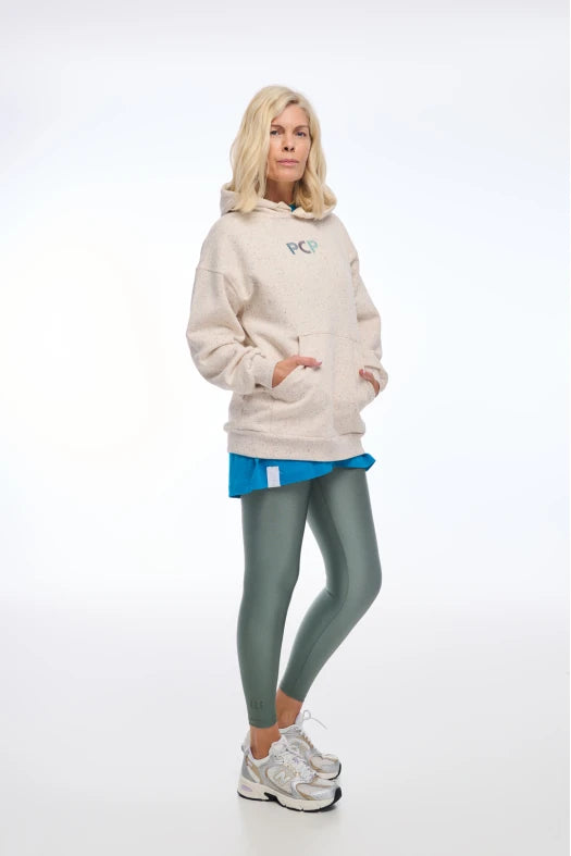 Woman wearing a beige hoodie with a logo, blue skirt, green leggings, and white sneakers on a white background
