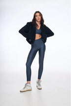 Woman wearing a black jacket, blue leggings, and white sneakers on a white background