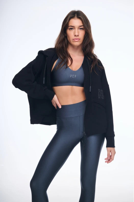 Woman wearing a black jacket, gray sports bra, and leggings on a white background