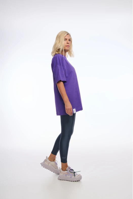 Person wearing a purple t-shirt and black leggings on a white background