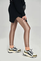 Person wearing bronze leggings and black sweater on a plain background