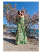 Woman in a green dress standing by a tree with pink blossoms near a body of water.