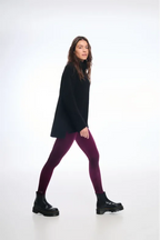 Person wearing a black poncho, purple leggings, and black boots on a white background