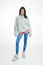 Person wearing a light gray oversized sweater with a pink shirt underneath, blue leggings, and white sneakers on a white background.