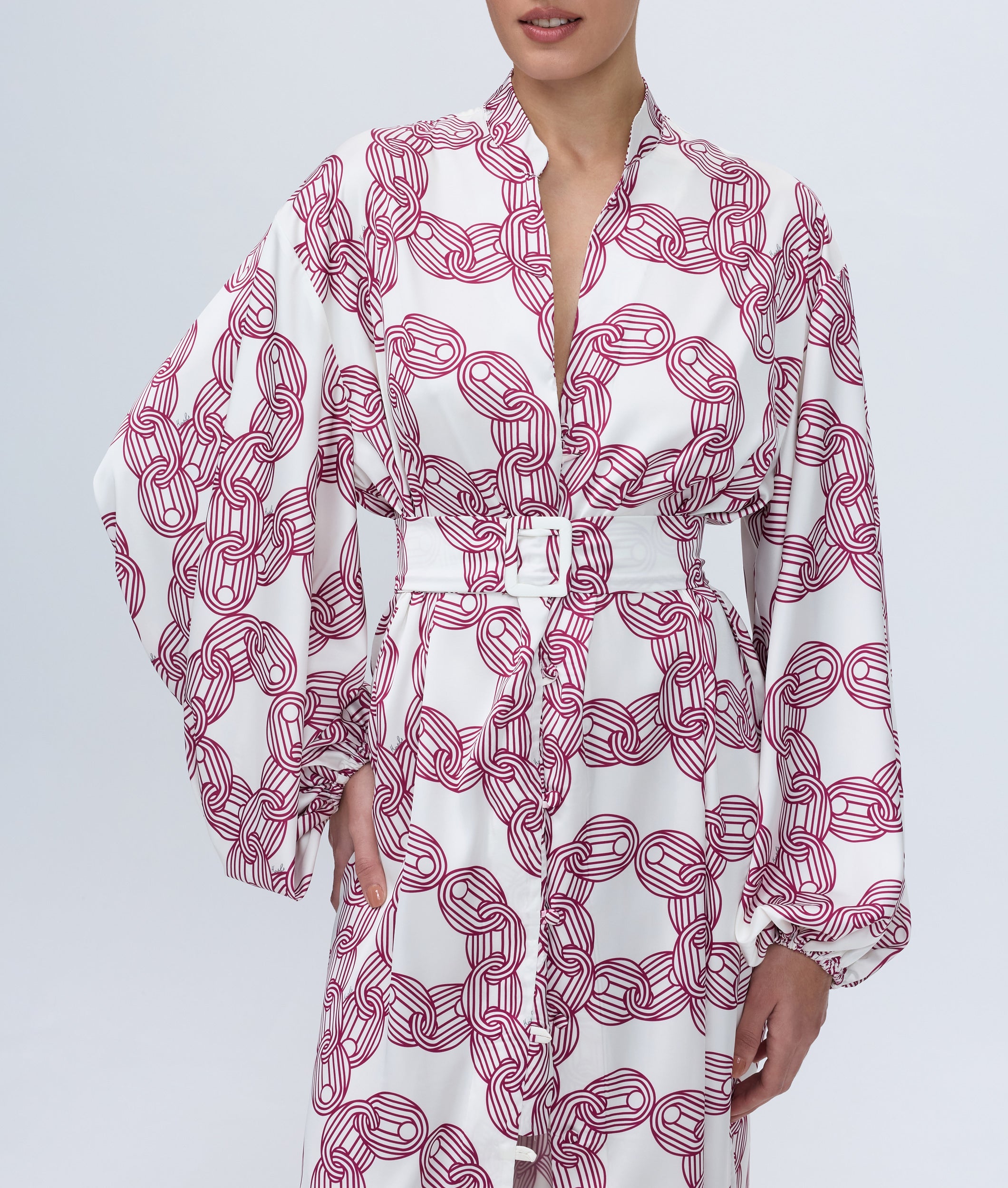 White dress with red chain pattern worn by a model on a light gray background