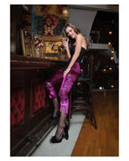 Woman in a bar setting wearing a black top and pink pants, holding a glass.
