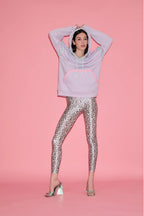 Person wearing a light purple hoodie and patterned leggings on a pink background