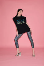 Woman wearing a black sleeveless top with text and graphics, paired with patterned leggings on a pink background