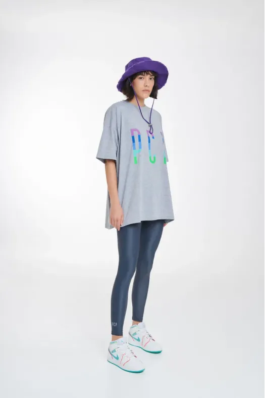 Person wearing a gray oversized t-shirt with colorful text, blue leggings, and a purple hat on a white background