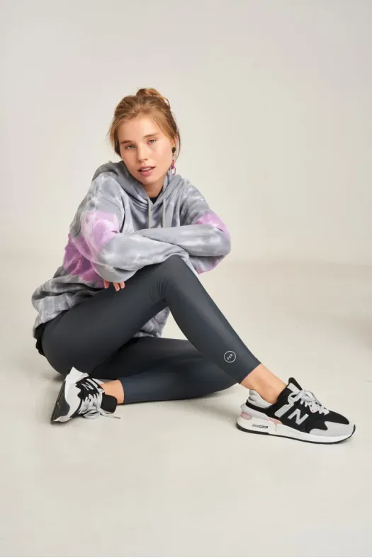 Person wearing a gray tie-dye hoodie, black leggings, and black sneakers on a light gray background