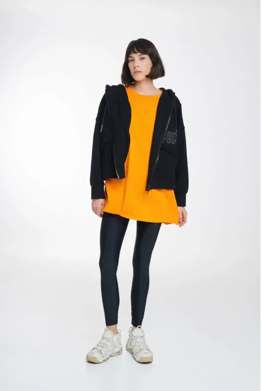 Person wearing a black hoodie over an orange dress with black leggings on a white background