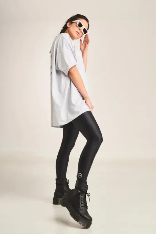 Person wearing a white oversized shirt, black leggings, and black boots on a plain background