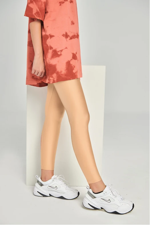 Person wearing a red tie-dye dress and white sneakers on a gray background