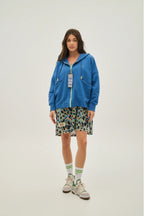 Person wearing a blue hoodie, patterned skirt, and sneakers on a white background