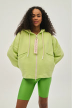 Person wearing a bright green hoodie and shorts with a visible brand tag on a white background