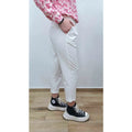Person wearing white pants and black sneakers with a pink floral top against a plain background