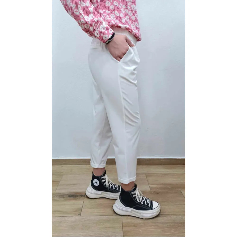 Person wearing white pants and black sneakers with a pink floral top against a plain background
