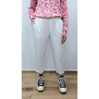 Person wearing a pink floral top, white pants, and black and white sneakers on a plain background