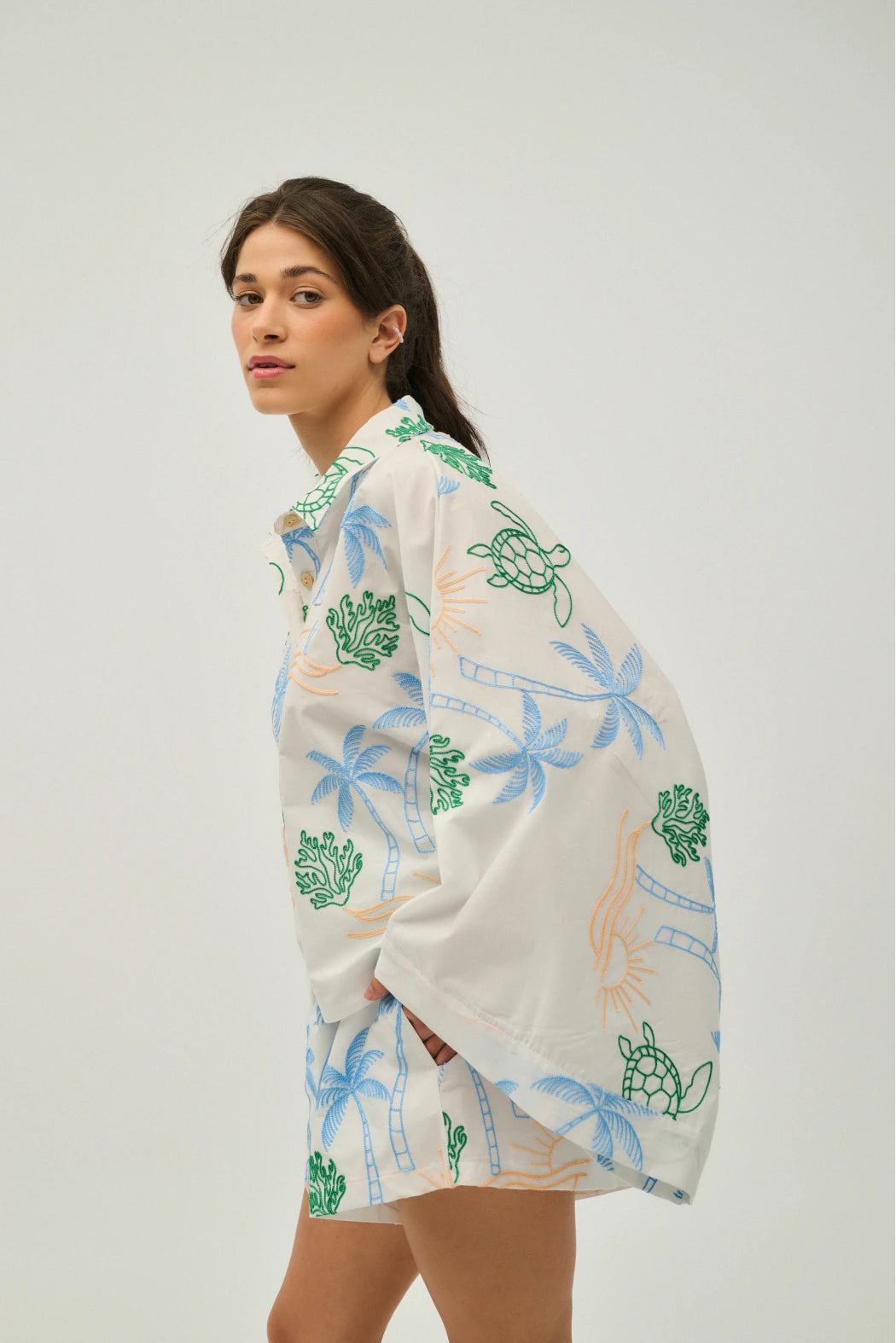 Woman wearing a white outfit with green and blue turtle designs on a plain background