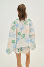 Person wearing a light-colored kimono-style garment with floral and turtle designs on a white background