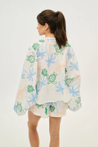 Woman wearing a light-colored blouse with floral and turtle designs on a white background