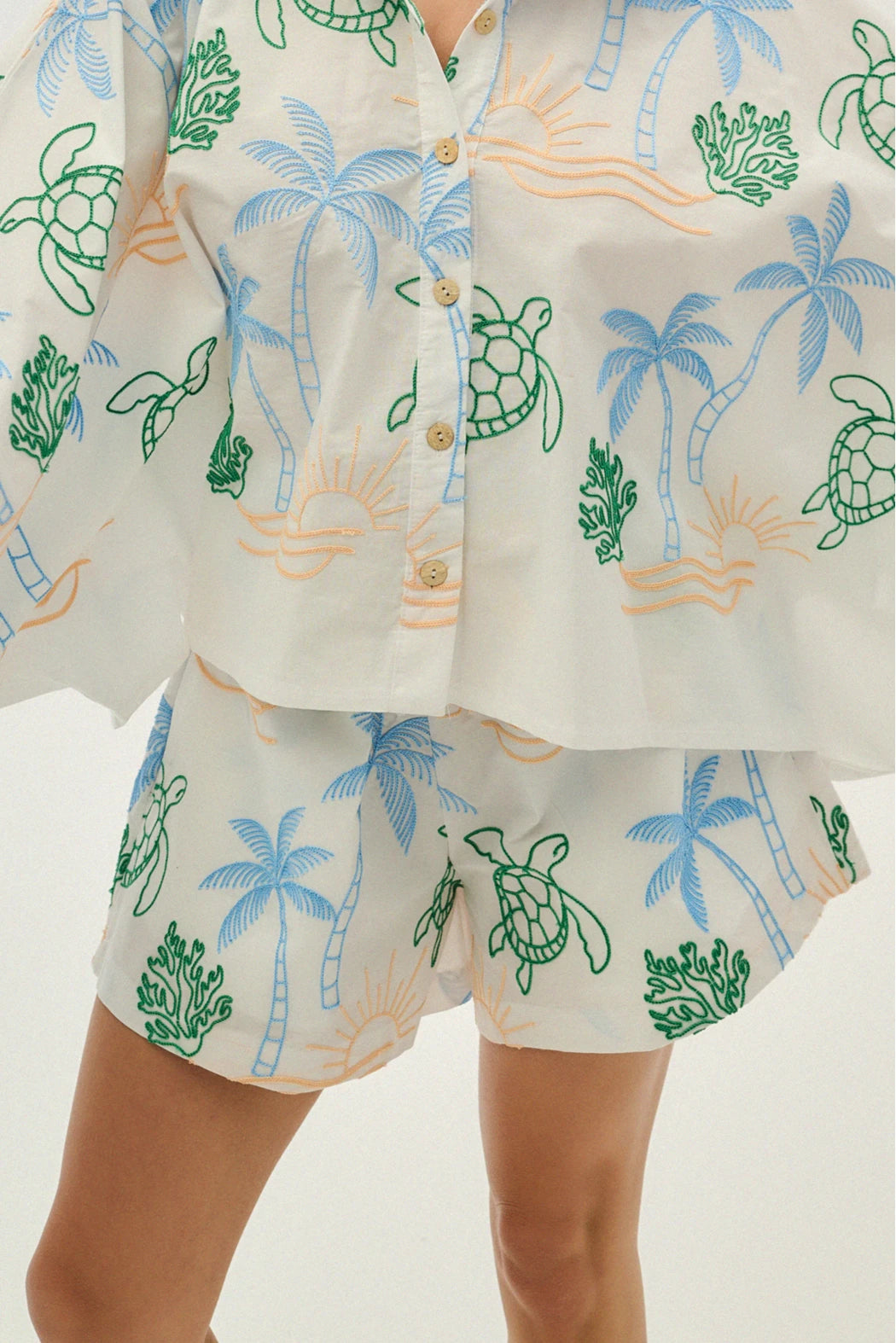 White shirt and shorts set with blue palm trees and green turtles on a white background
