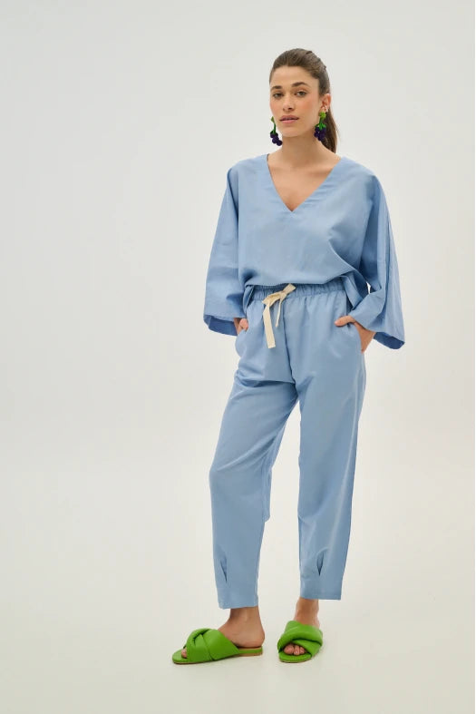 Woman wearing a light blue outfit with green slippers on a white background
