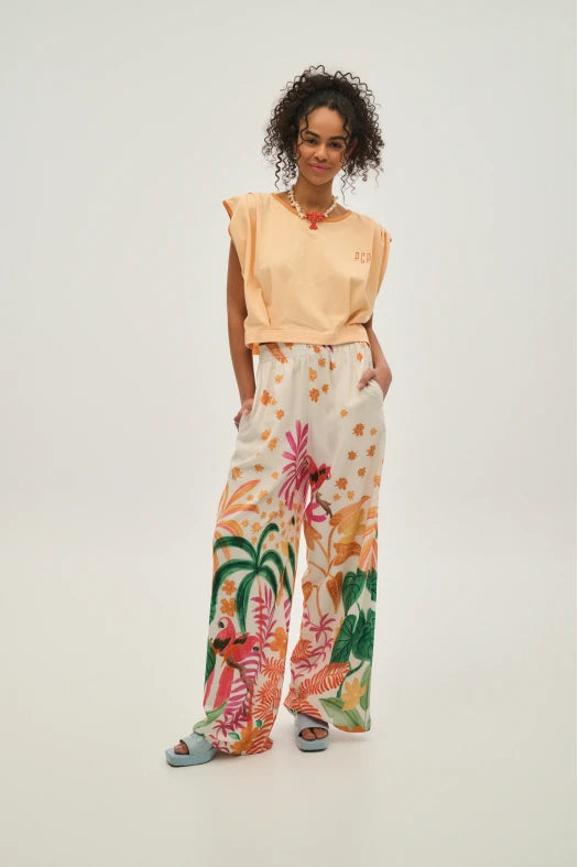 Woman wearing a peach top and floral pants on a white background