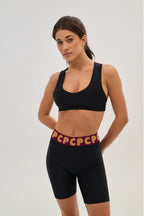 Woman wearing a black sports bra and shorts with a red waistband on a light gray background