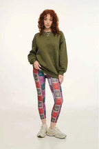 Person wearing a green oversized sweatshirt and patterned leggings on a white background