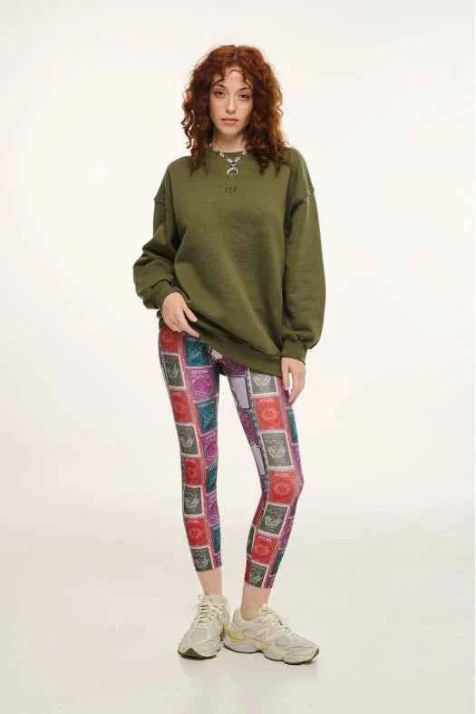 Person wearing a green oversized sweatshirt and patterned leggings on a white background