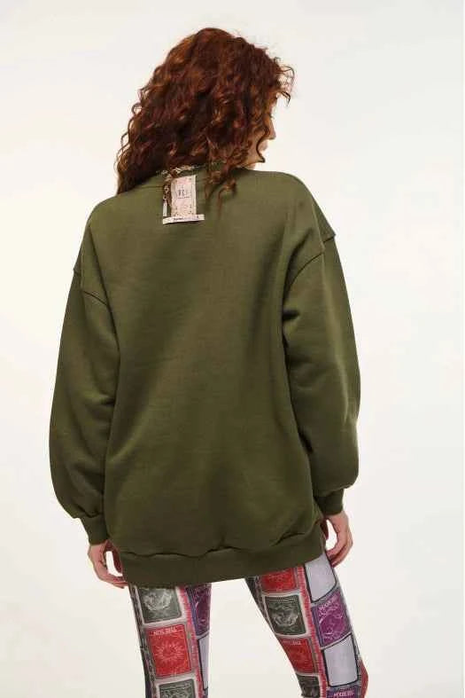 Person wearing a green sweatshirt with a patch on the back, standing against a white background.