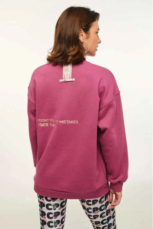 Person wearing a pink sweatshirt with text on the back, standing against a white background