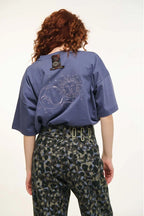 Person wearing a blue shirt with a sun and moon design on the back, standing against a white background.