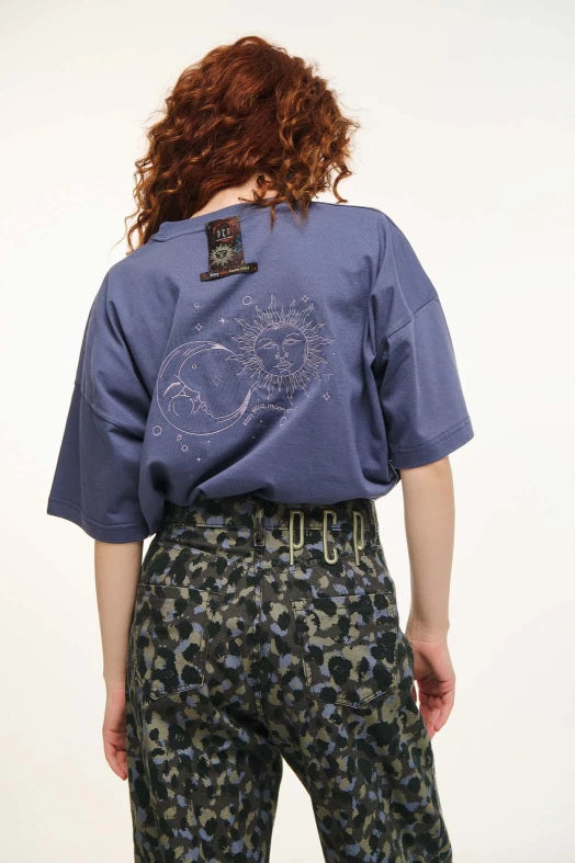Person wearing a blue shirt with a sun and moon design on the back, standing against a white background.