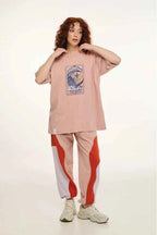 Person wearing a pink oversized t-shirt with a graphic design and pink pants with red and white stripes on a light background
