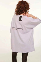 Person wearing a light purple oversized t-shirt with text on the back against a white background