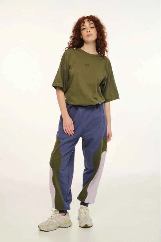 Person wearing a green oversized shirt and blue pants with color blocking on a white background