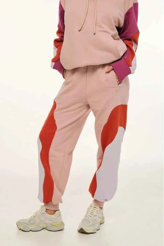 Person wearing a pink and red tracksuit with white sneakers on a light background