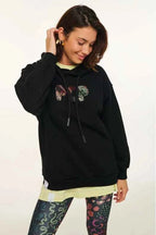 Person wearing a black hoodie with colorful designs and patterned leggings on a white background