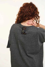 Person wearing a gray t-shirt with a brand logo on the back, against a plain background