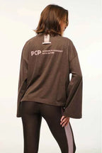 Person wearing a brown long-sleeve shirt with 'PCP' branding on the back, standing against a plain background.