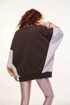 Person wearing a two-tone sweater with one sleeve black and the other white on a plain background