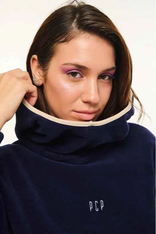 Person wearing a navy blue sweater with a high collar and 'PCP' logo.