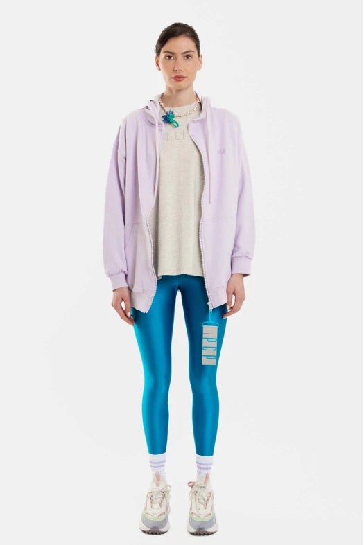 Person wearing a light purple jacket, beige sweater, blue leggings, and white sneakers on a white background