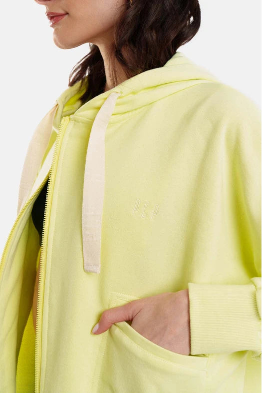 Person wearing a light green jacket with a white zipper on a plain background